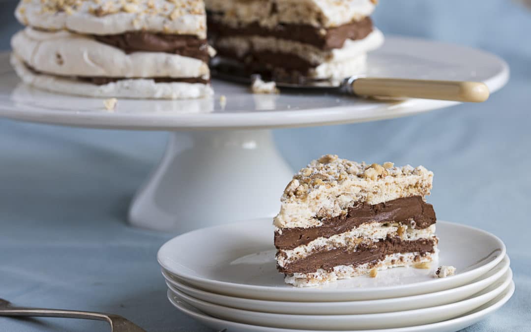 a three tiered cake made with layers of hazelnut meringue, sandwiched together with a chocolate cream and topped with toasted hazelnuts