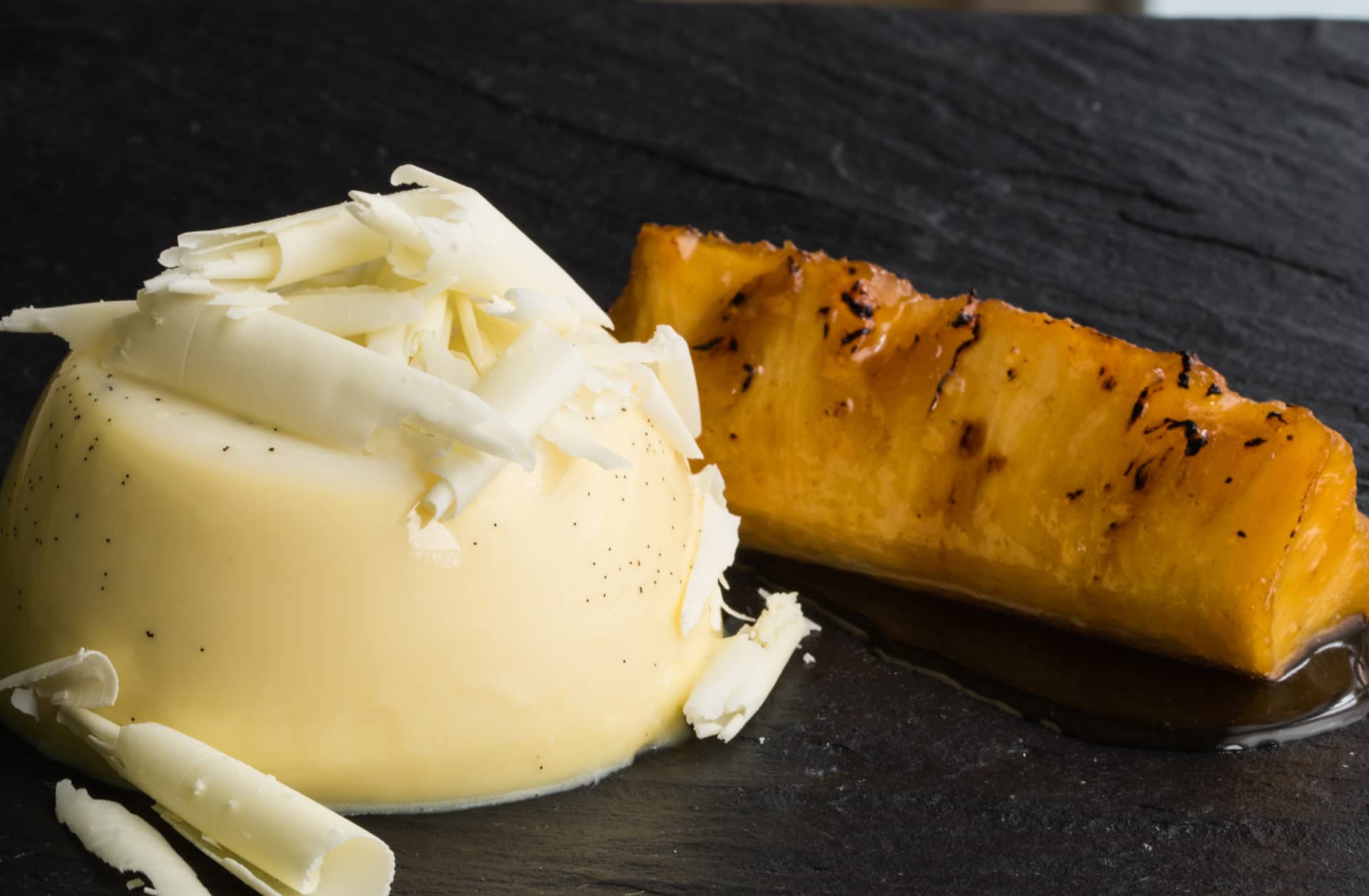 A white chocolate panna cotta, topped with white chocolate shavings, and served with roast pineapple