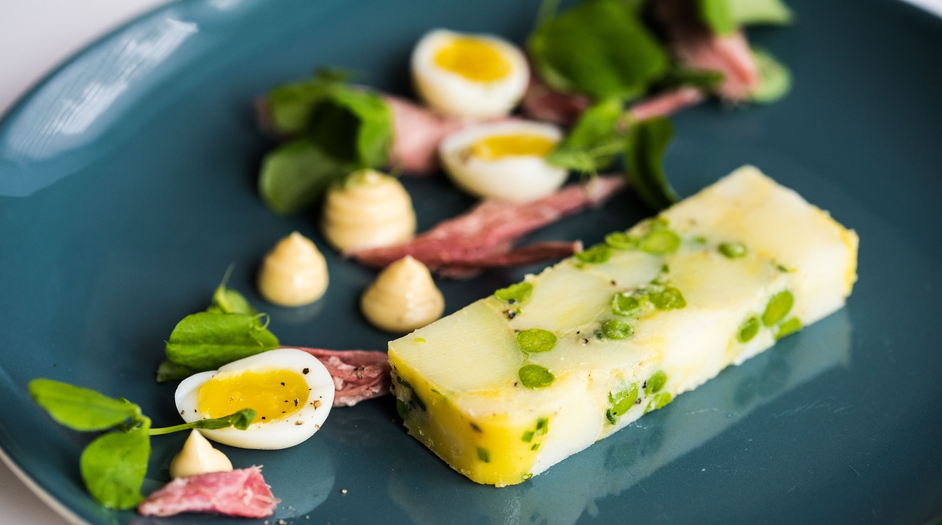 a slice of terrine, made with new potatoes, peas, chives and set with butter, served with ham hock and quails eggs