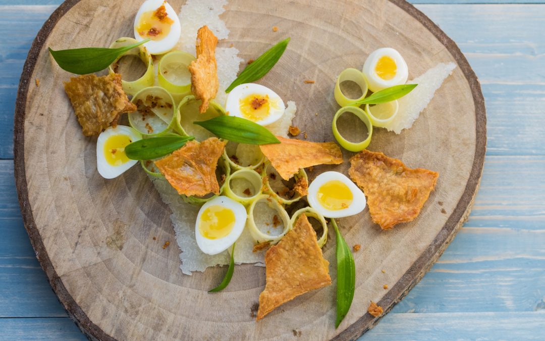 A salad of sliced leeks, wild garlic leaves, soft boiled quails eggs and chicken skin crackling served on a wooden platter