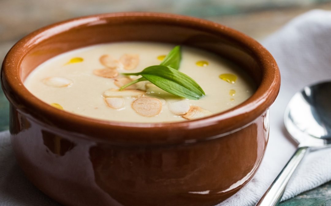 A terracotta bowl of creamy roast garlic soup garnished with a wild garlic leaf