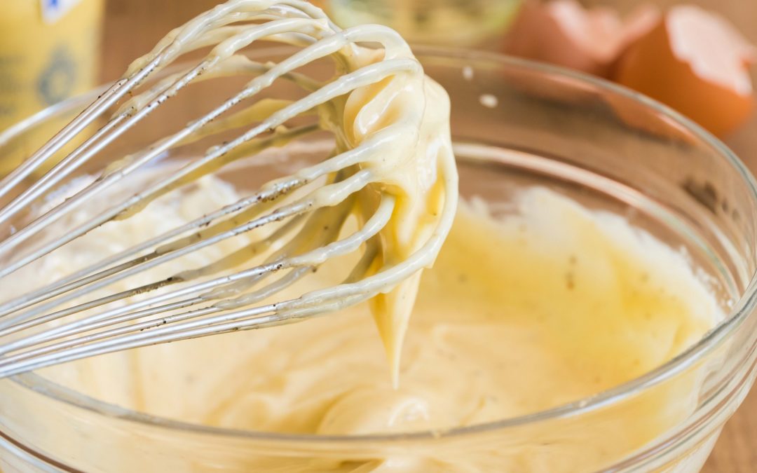 Thick home-made mayonnaise drips from a whisk into a bowl of yellow mayonnaise