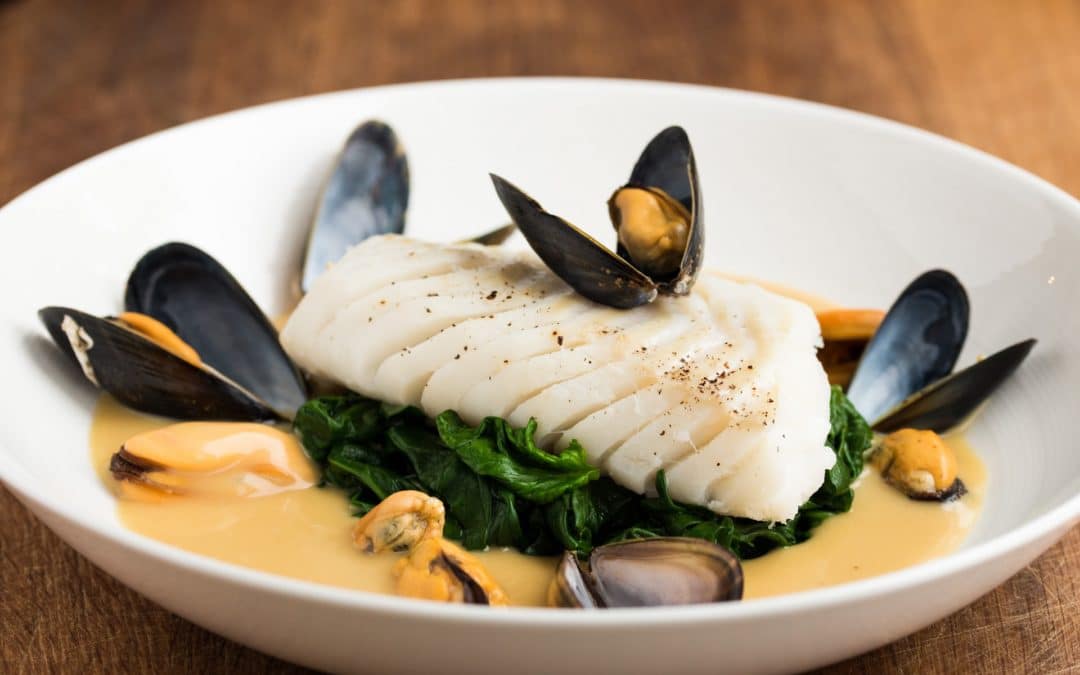 Opened mussles sit on top of white flakes of cod, with a bed of wilted spinach and an orange mussel sauce