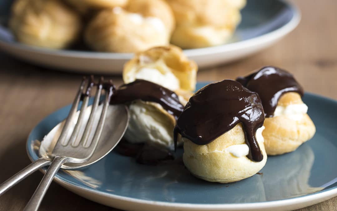 Profiteroles with melting chocolate sauce poured over cream filled choux buns