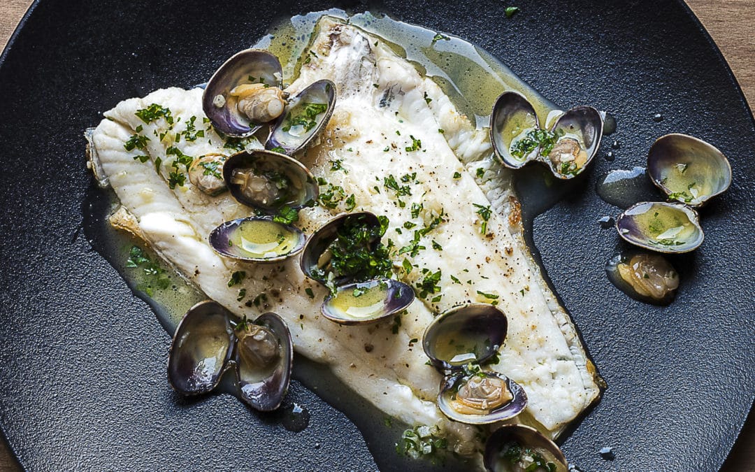 A white fillet of grilled plaice served with a sauce made with clams and garlic and parsley is poured over it
