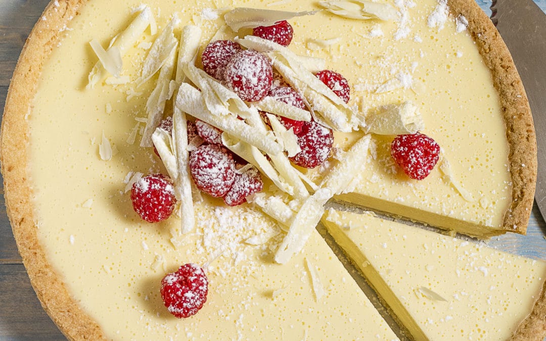A dessert of white chocolate tart topped with fresh raspberries, shavings of white chocolate and dusted with icing sugar