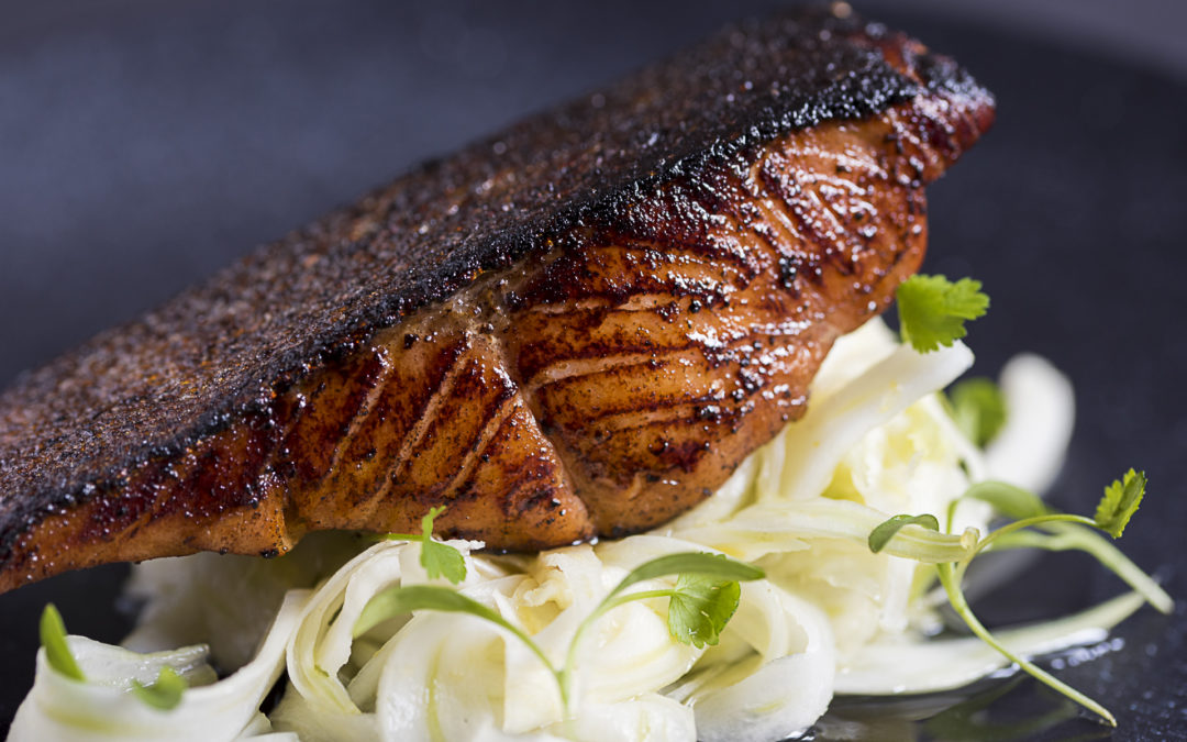 A fillet of blackened pan fried salmon sits on top of a salad of fennel